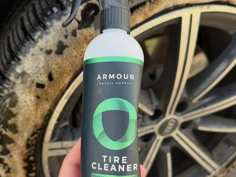 Botella de Armour Tire Cleaner junto a rin sucio